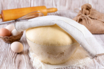 Fresh yeast dough for pizza, bread, baguettes, sourdough on wooden table. Yeast dough in a glass bowl